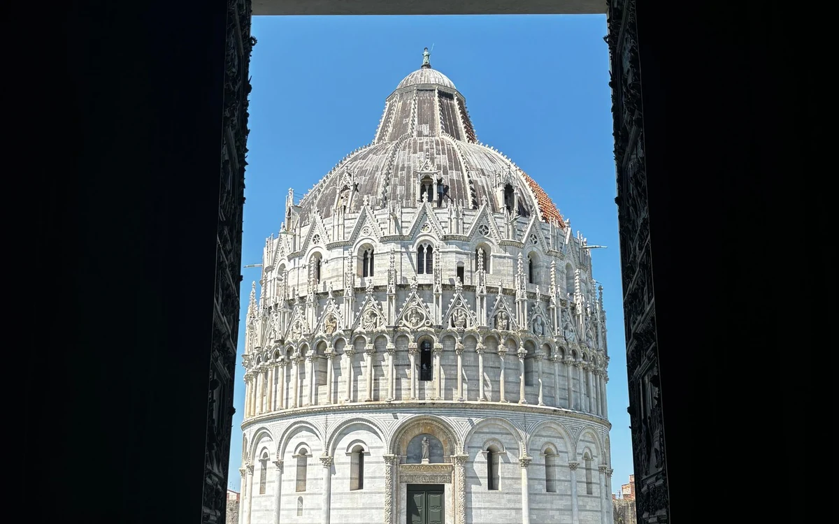 The round marble Baptistery of Pisa seen through a dark doorway