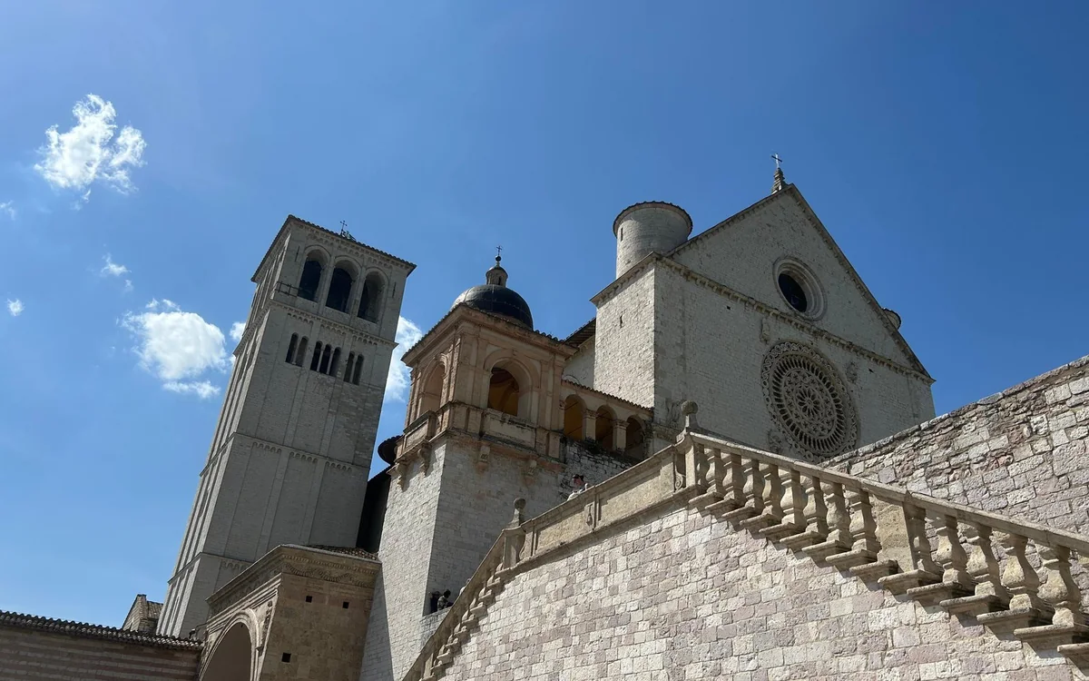 The Upper Basilica of Saint Francis in Assisi with its rose window and bell tower, a stone balustrade in front, under a blue sky