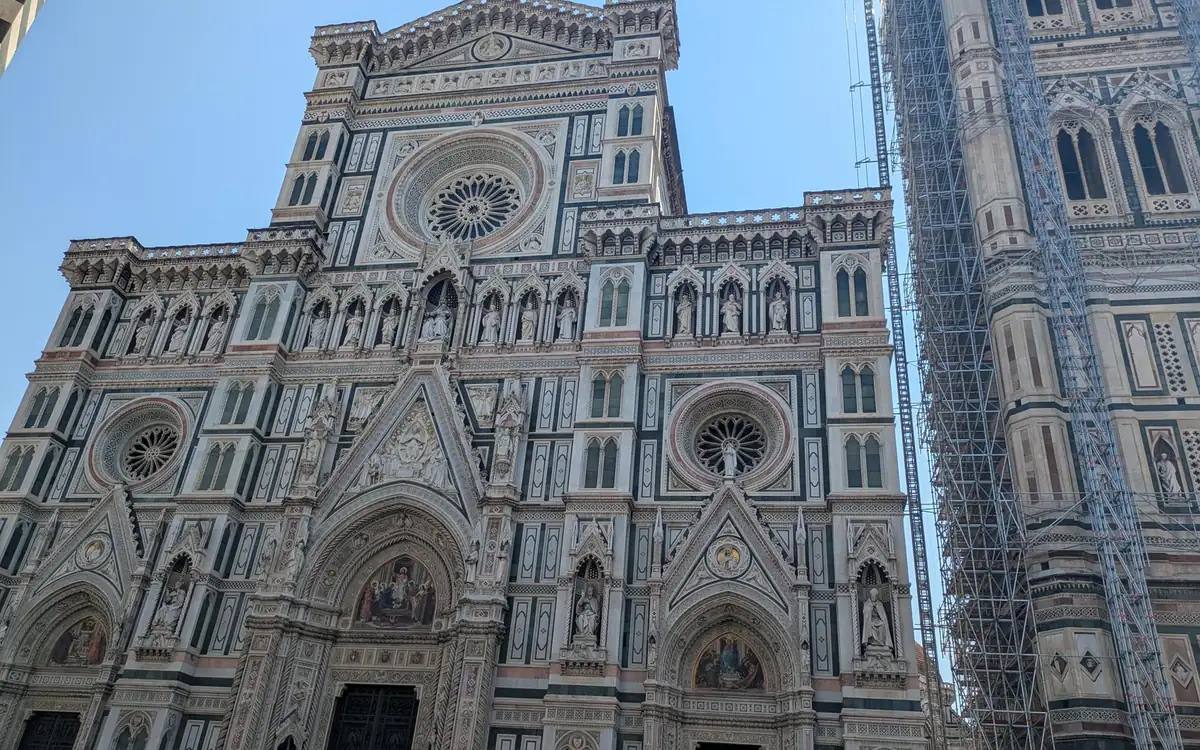 The marble front of Florence Cathedral with round windows, the bell tower in scaffolding