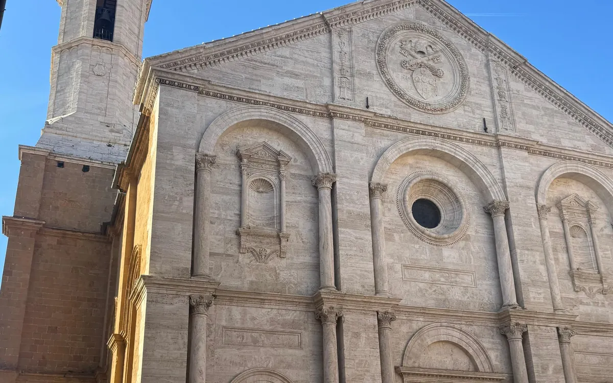 A pale stone church front with round arches and a bell tower