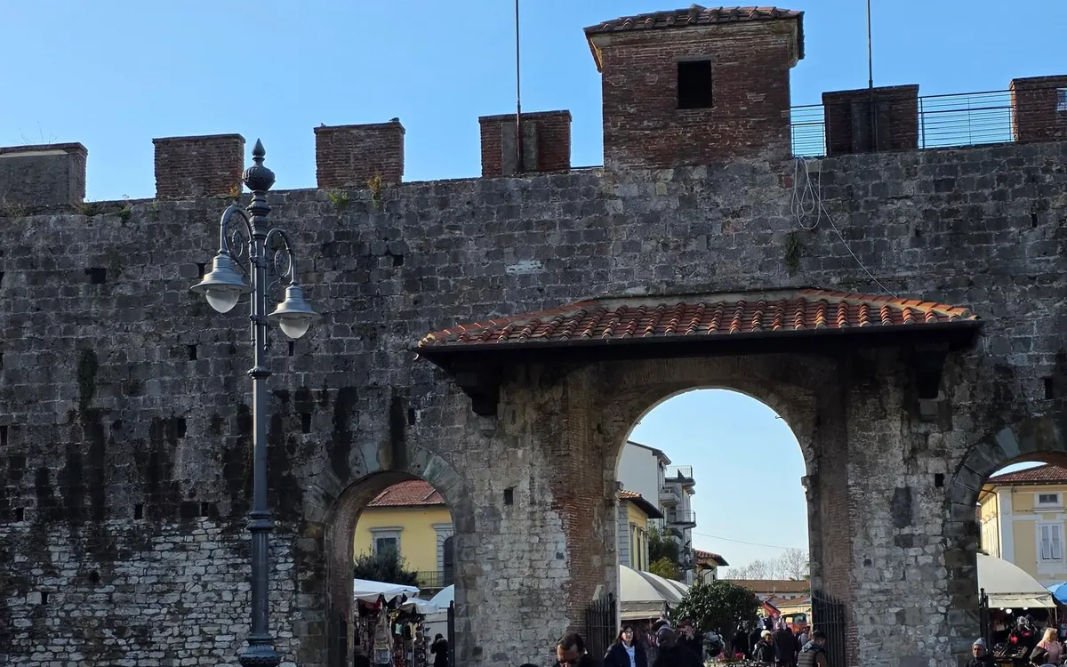 A gate in old stone walls, battlements above and a tiled roof over the arch