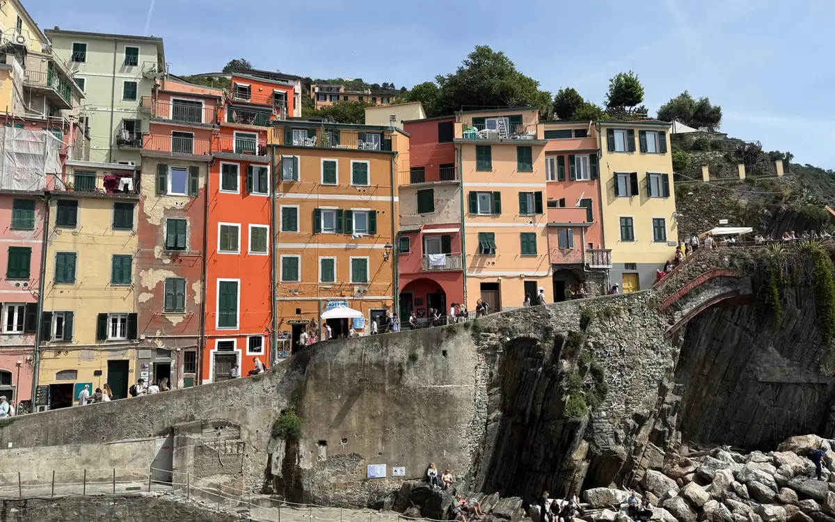 Tall houses in orange, yellow and pink above a stone sea wall and rocks
