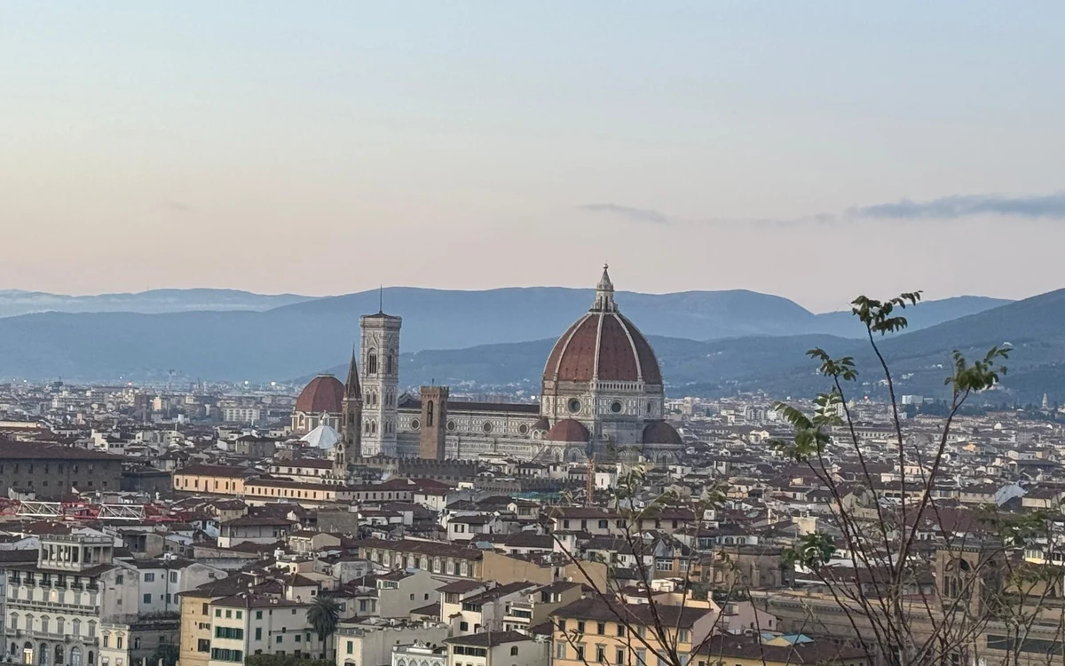 The dome of Florence cathedral and its bell tower rising over the rooftops at dusk, hills behind