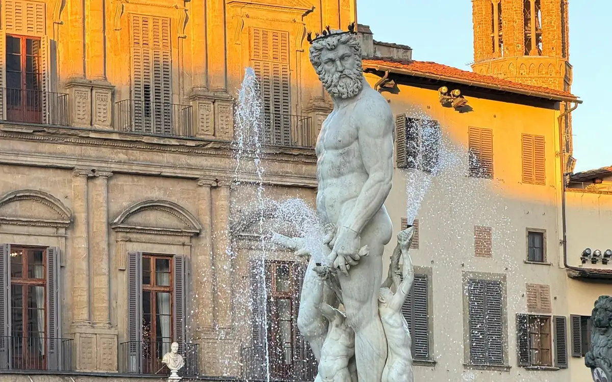 A marble sea god on a Florence fountain, water jets and palace fronts in golden light