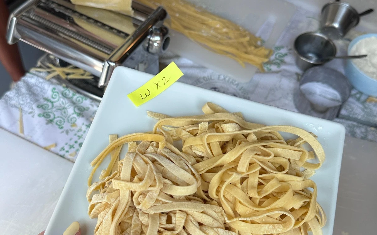 Fresh ribbon pasta on a white plate, a pasta machine behind