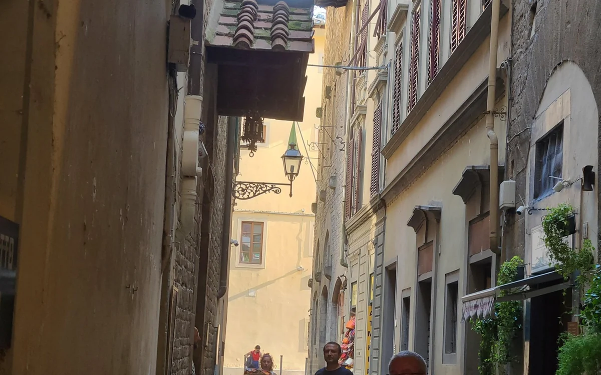 A narrow lane in central Florence, a lantern and shuttered windows above people walking