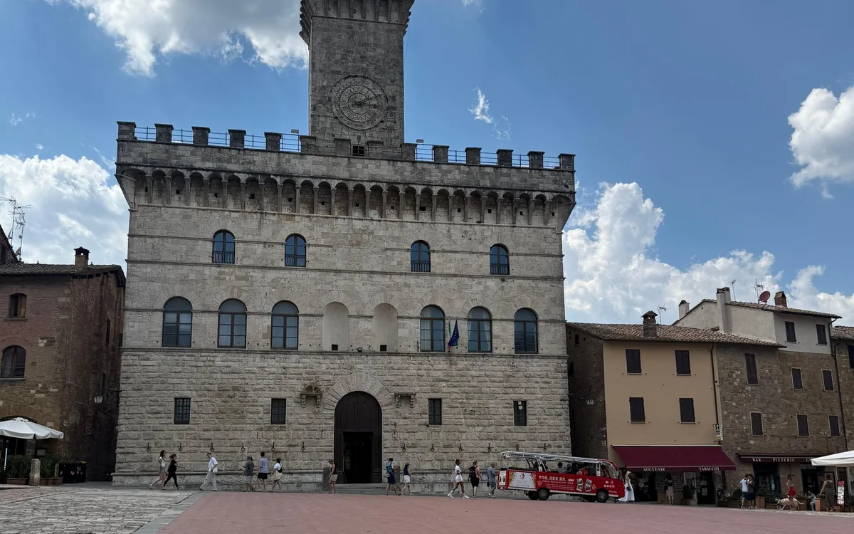A stone palazzo with battlements and a clock tower on a wide square