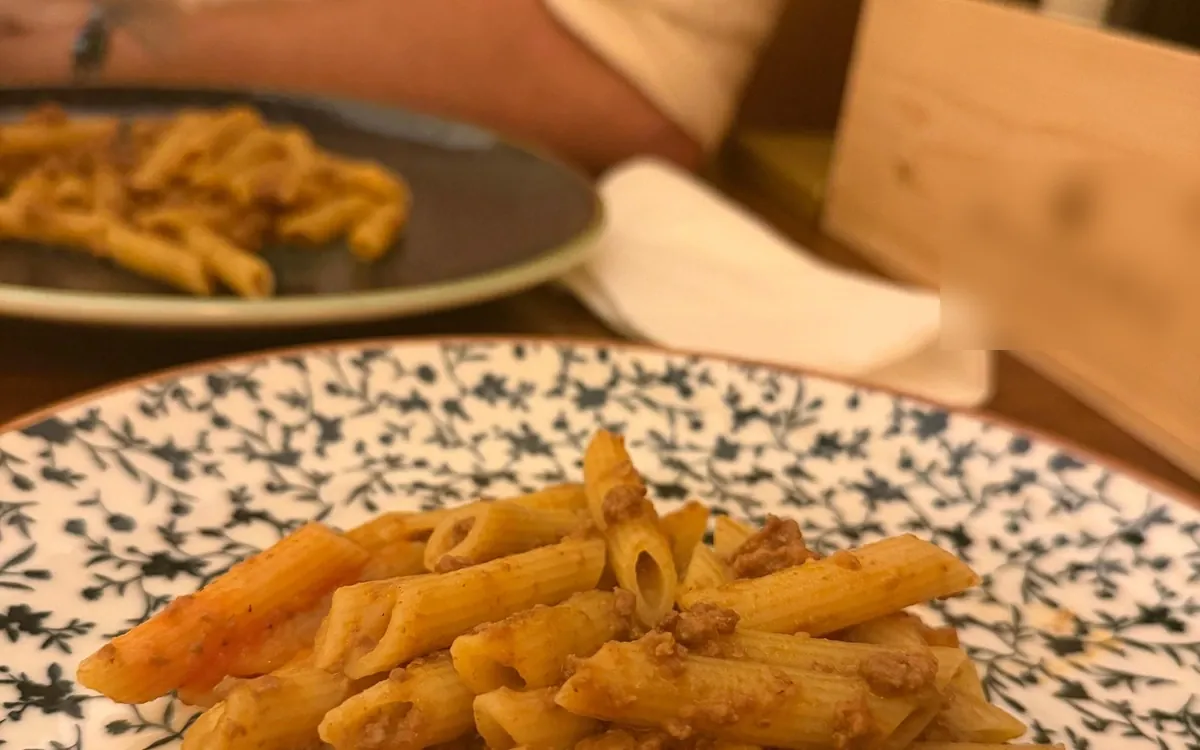 Penne with a meat sauce in a bowl with a blue pattern, a second plate behind