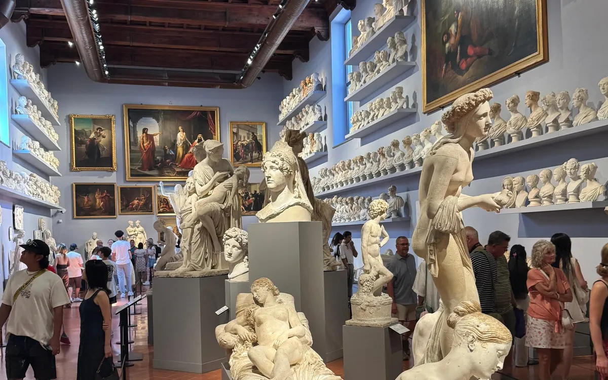 A hall with shelves of white busts, statues on plinths and paintings