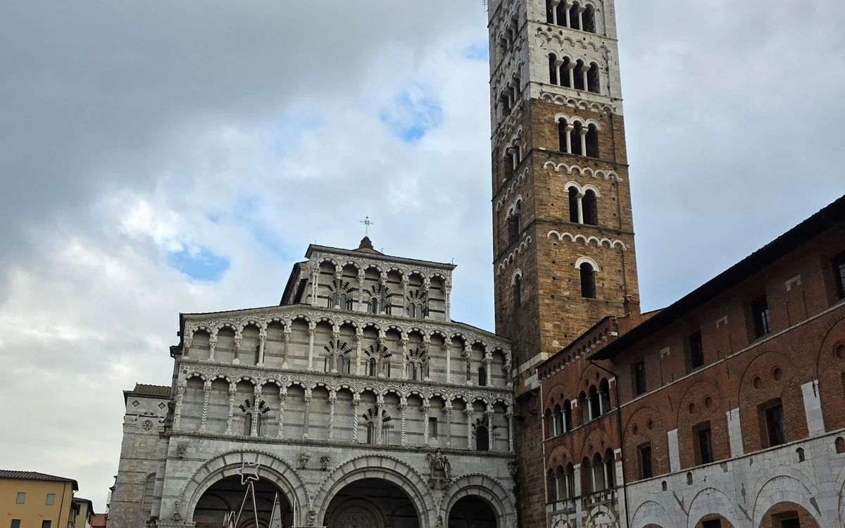 A Romanesque church front with tiers of marble arches beside a brick bell tower