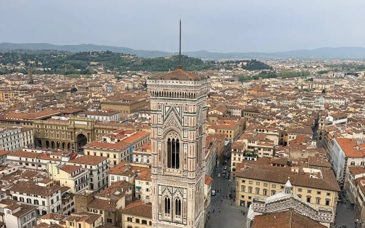 The striped marble bell tower seen from high above, red roofs and green hills behind