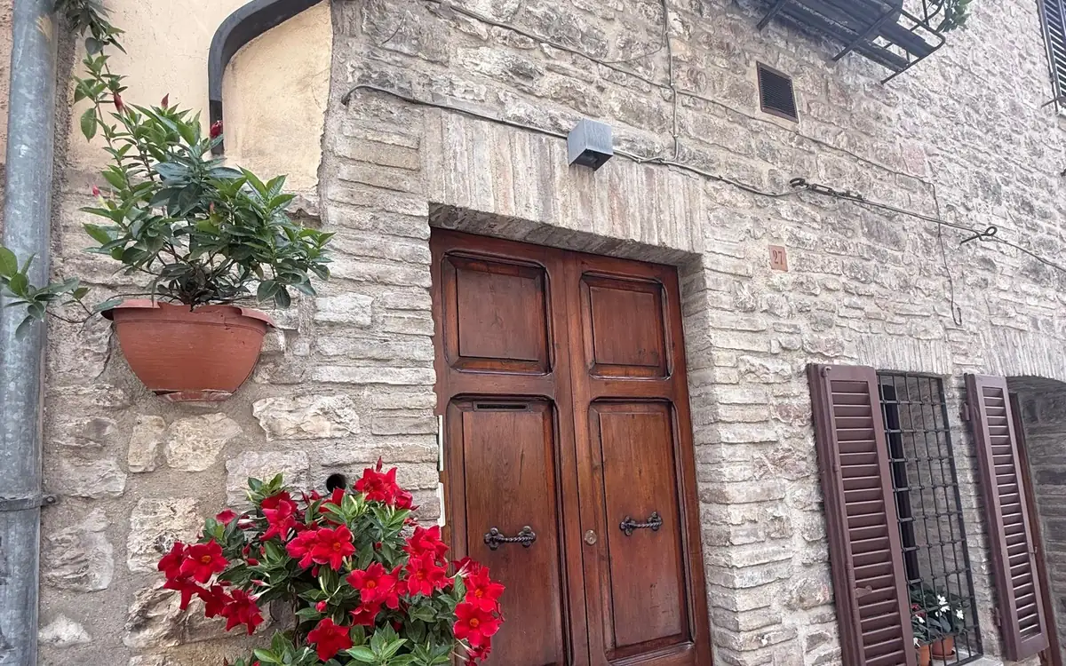 A wooden door in a stone wall in Assisi, red flowers in front
