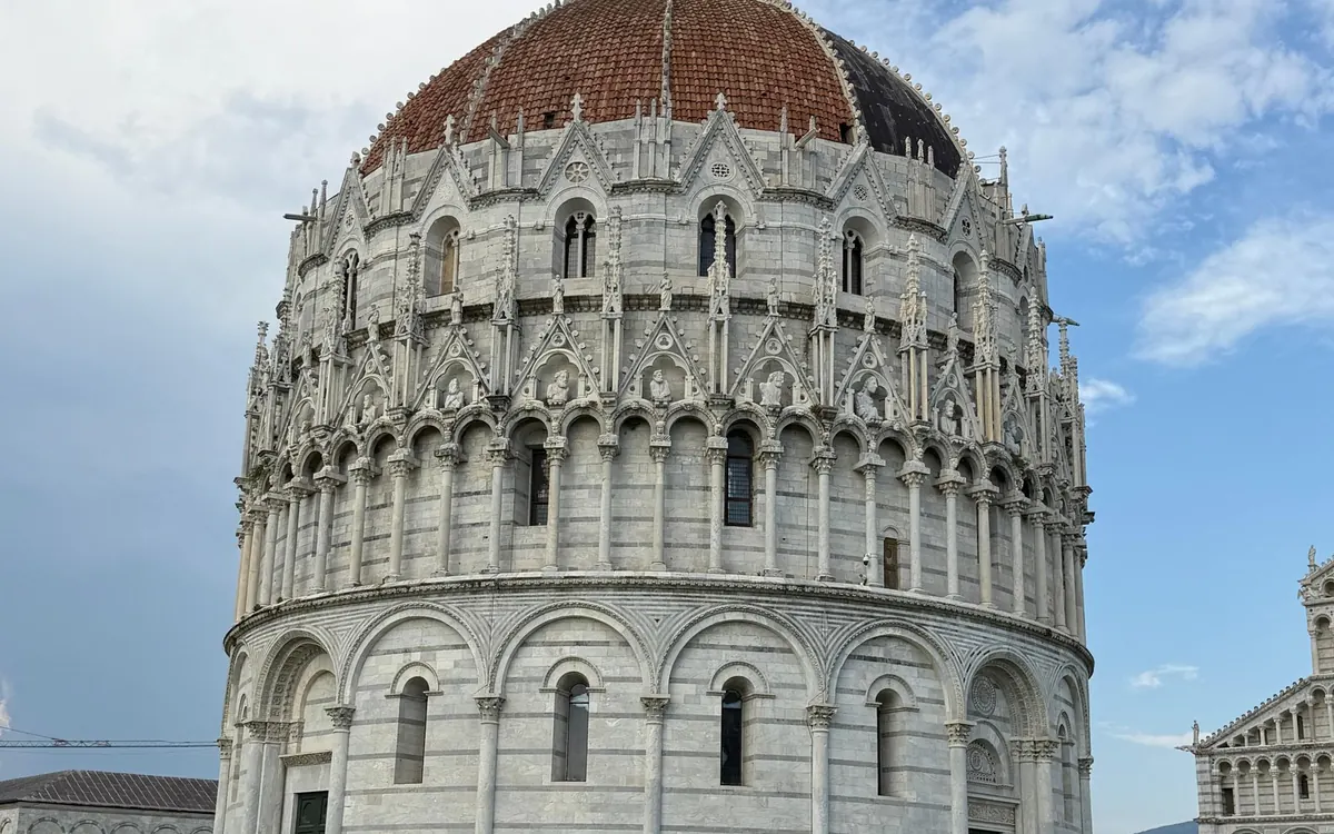 The round marble Baptistery of Pisa under its red dome, the cathedral at the edge of the frame