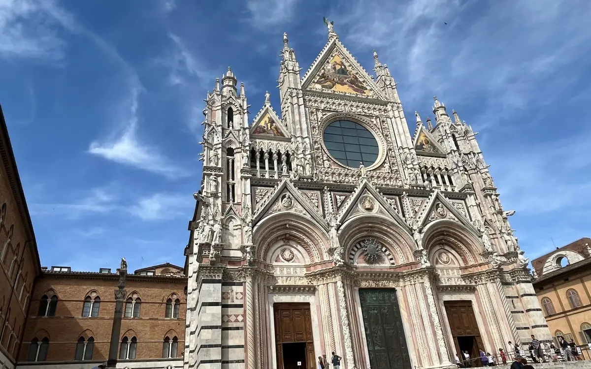 The Gothic marble front of Siena Cathedral, its rose window and gilded gables against a blue sky