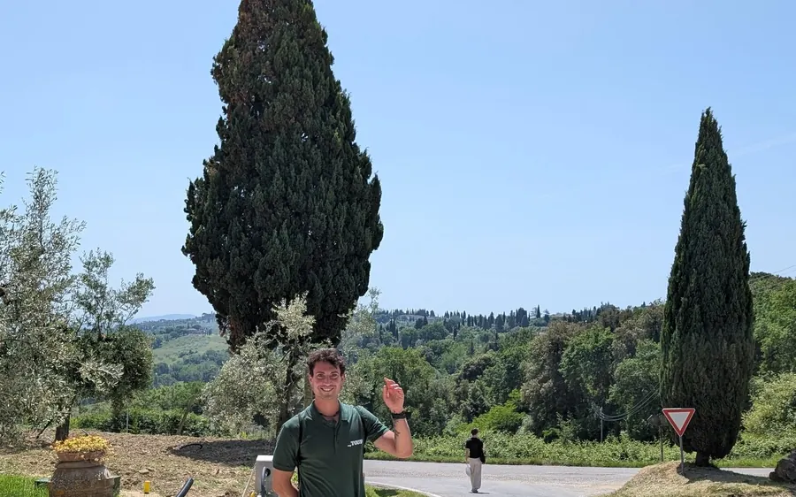 A man waving by a country road between tall cypress trees
