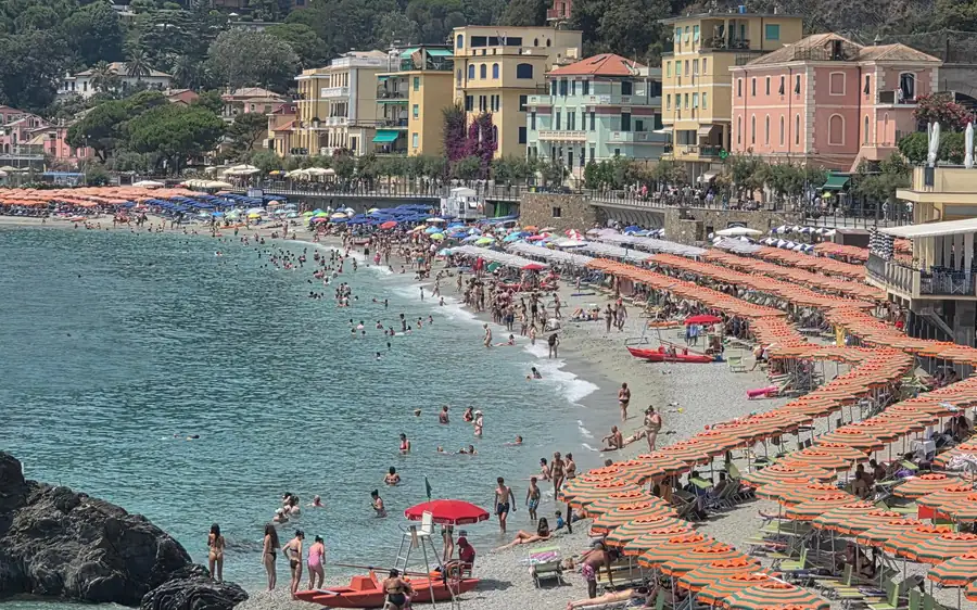 Orange beach umbrellas below colourful seafront houses on the Ligurian coast