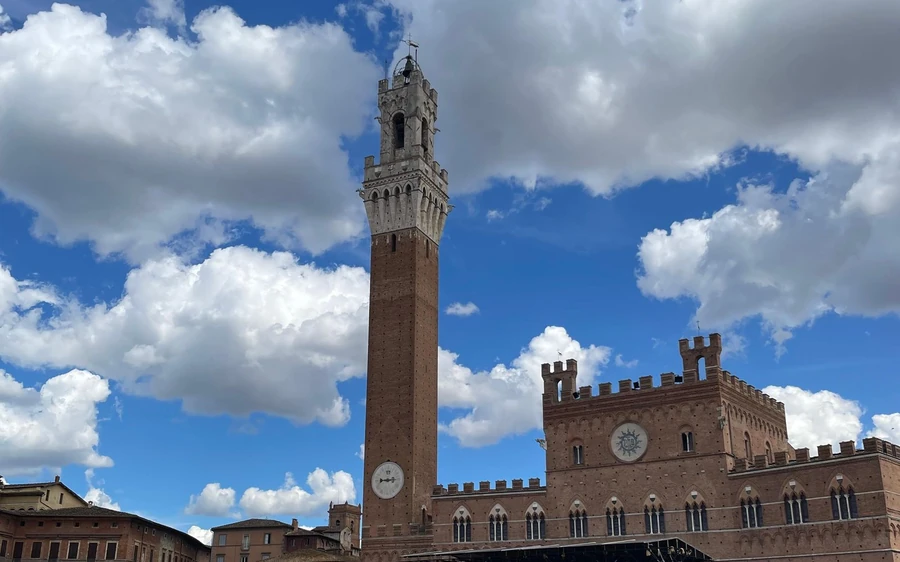 A tall brick tower beside a crenellated town hall under a cloudy sky