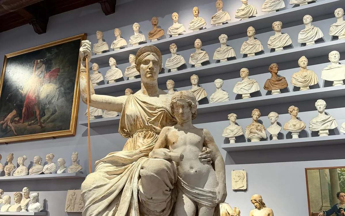 A draped figure with a staff and a child, busts on shelves behind
