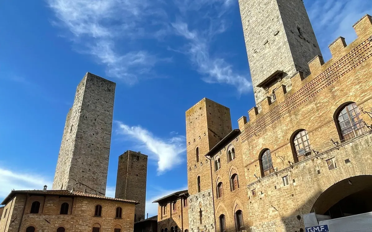 Stone towers and a battlemented palace in San Gimignano under a blue sky