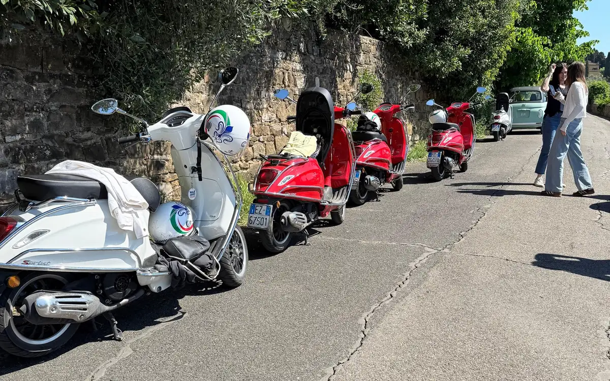 A white Vespa and four red ones parked along a stone wall